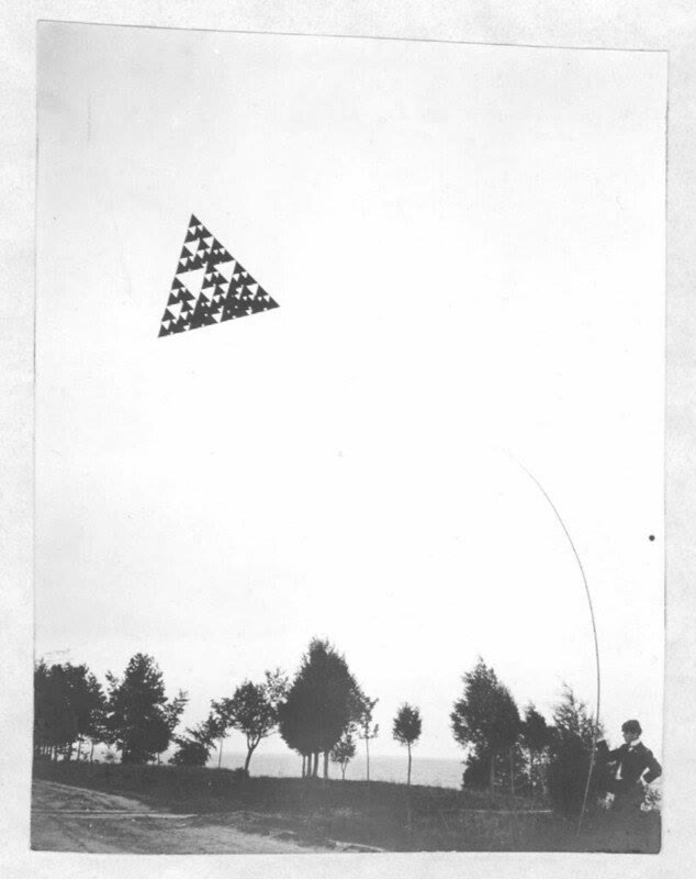 A triangular tetrahedral kite flying high above a field